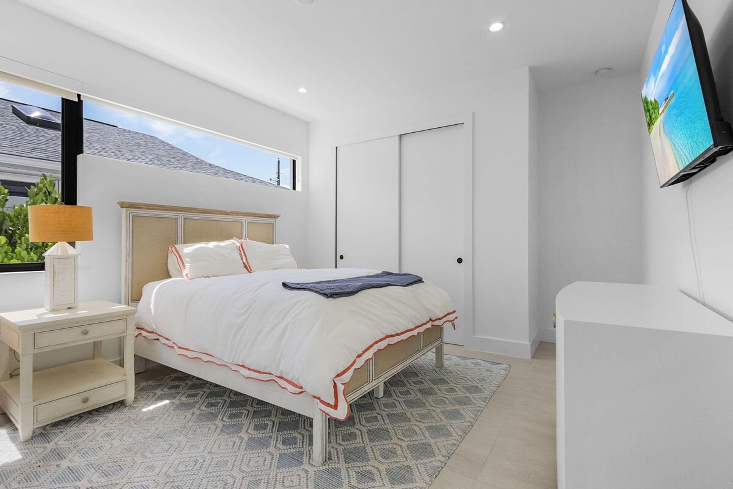 A modern bedroom with a bed, bedside table, lamp, and a TV mounted on the wall.