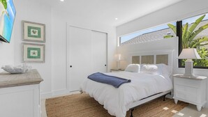 Une chambre moderne avec un lit, des tables de chevet, un téléviseur et une fenêtre donnant sur un paysage verdoyant.