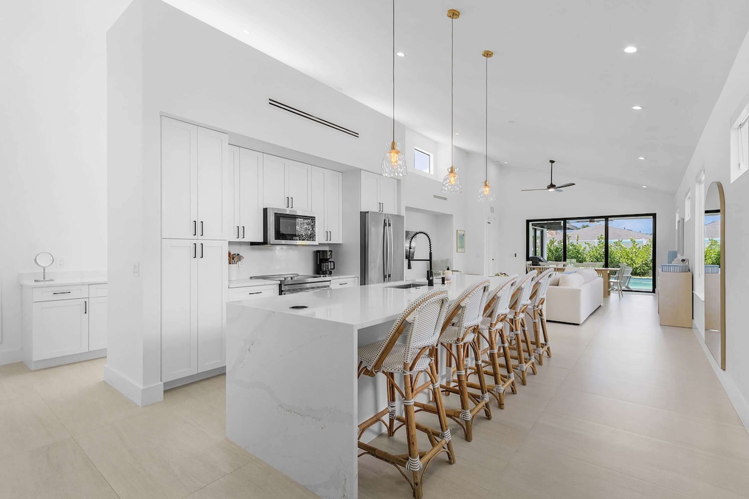 A modern kitchen with white cabinetry, a marble island, and a dining area with wicker chairs.