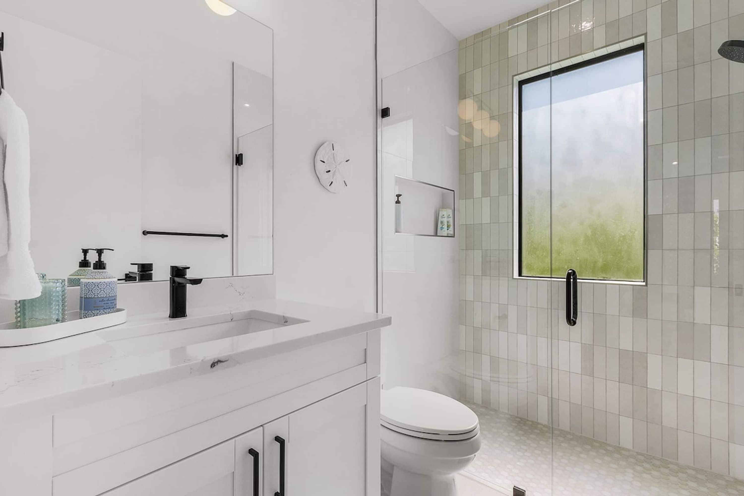 A modern bathroom with a large mirror, a sink with a faucet, a toilet, and a shower area.