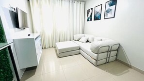 Ein modernes Wohnzimmer mit einem Ecksofa, einem Flachbildfernseher und einer kleinen Kommode.
