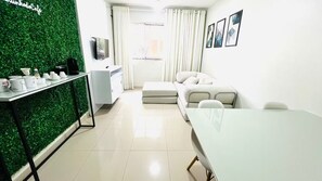 Un salon moderne avec un mur vert, une table à manger, un canapé et un téléviseur.