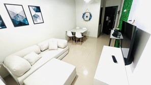 A modern living room with a white sofa, a dining table with chairs, a flat-screen TV mounted on the wall, and a small table with a remote control. - EstadiaLimpa - Refuge in the 216 North area, in a residential building with 24-hour security. (Asa Norte, Brasília)