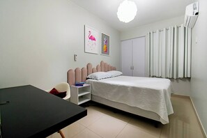 Ein Schlafzimmer mit Bett, Schreibtisch, Stuhl, Kleiderschrank und einem Fenster mit Vorhängen.
