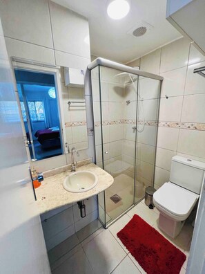 Ein Badezimmer mit einer gläsernen Duschkabine, einem weißen Waschbecken und einer Toilette.