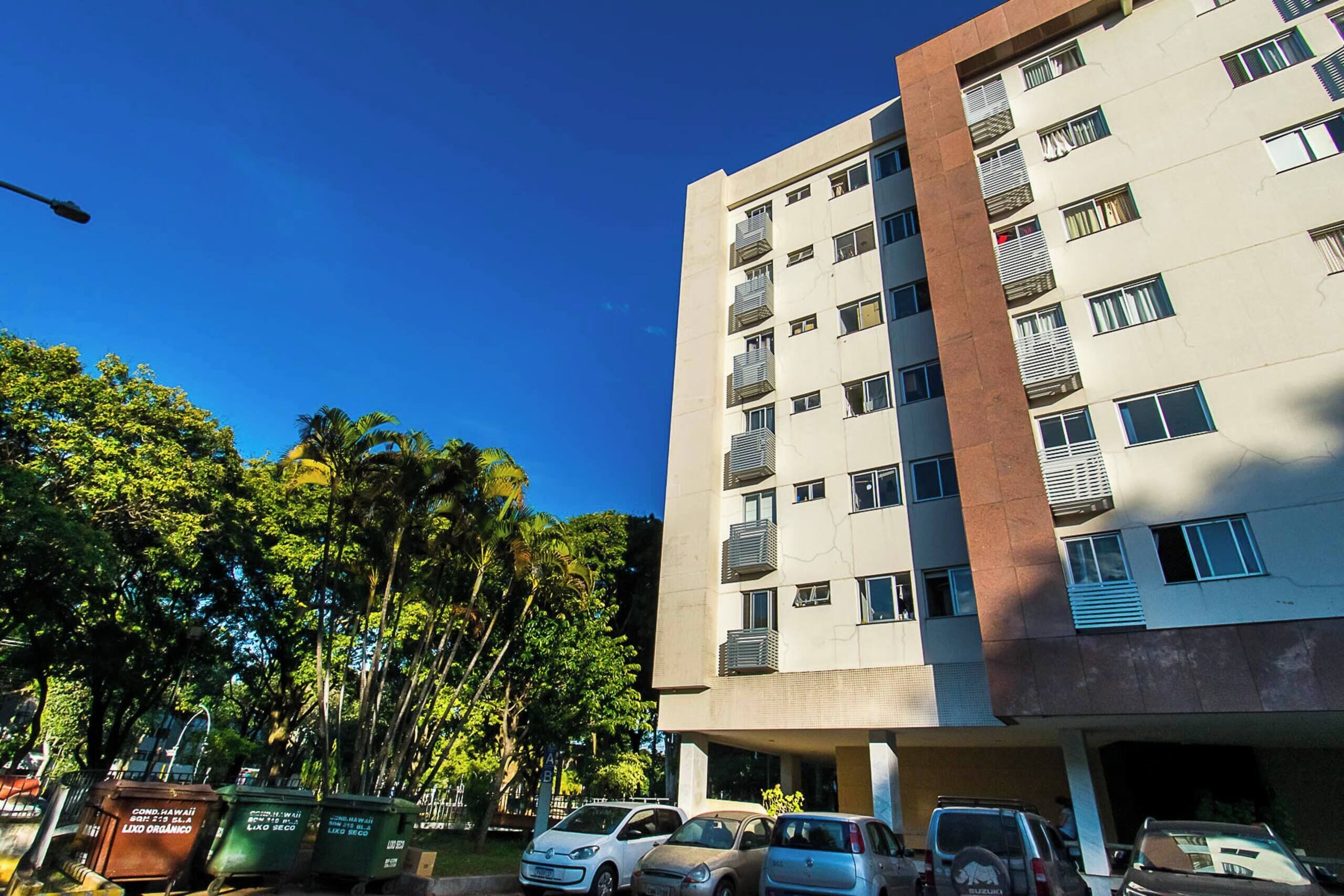Un edificio a più piani con balconi, auto parcheggiate e alberi.