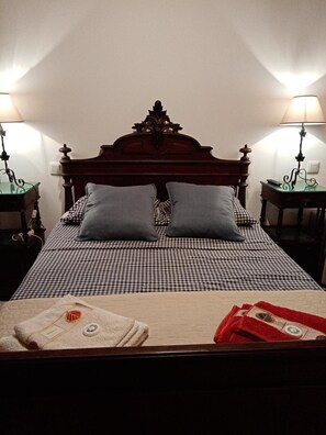 Una cama con colcha a cuadros, dos almohadas, un cabecero de madera y dos mesitas de noche con lámparas.