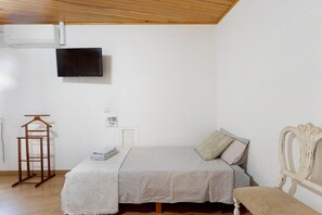 Een slaapkamer met een bed, een aan de muur bevestigde televisie, een houten kleerhanger en een nachtkastje.