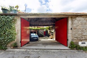 A garage entrance with a car parked inside, a stone wall, and a red door.