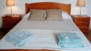 A double bed with a wooden headboard, two bedside tables with lamps, and folded towels on the bed. - Pêssego - Al Apartment with Mountain View, Wi-Fi, and Air Conditioning (Belece)