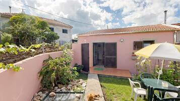 Una propiedad residencial con fachada rosa, techo de tejas, un pequeño jardín y un gato, además de mobiliario de exterior.