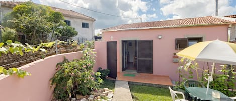 Una propiedad residencial con fachada rosa, techo de tejas, un pequeño jardín y un gato, además de mobiliario de exterior.