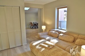 A living room with a sofa, a table, and a lamp. There is a window and a door. - NEW! Creekside Lounging. Downtown Manitou Springs. 2 BR/2 BA. A/C. New Hot Tub! (Manitou Springs)