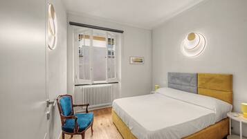 Ein Schlafzimmer mit Bett, Sessel, Heizkörper, Fenster und einer Wandleuchte.