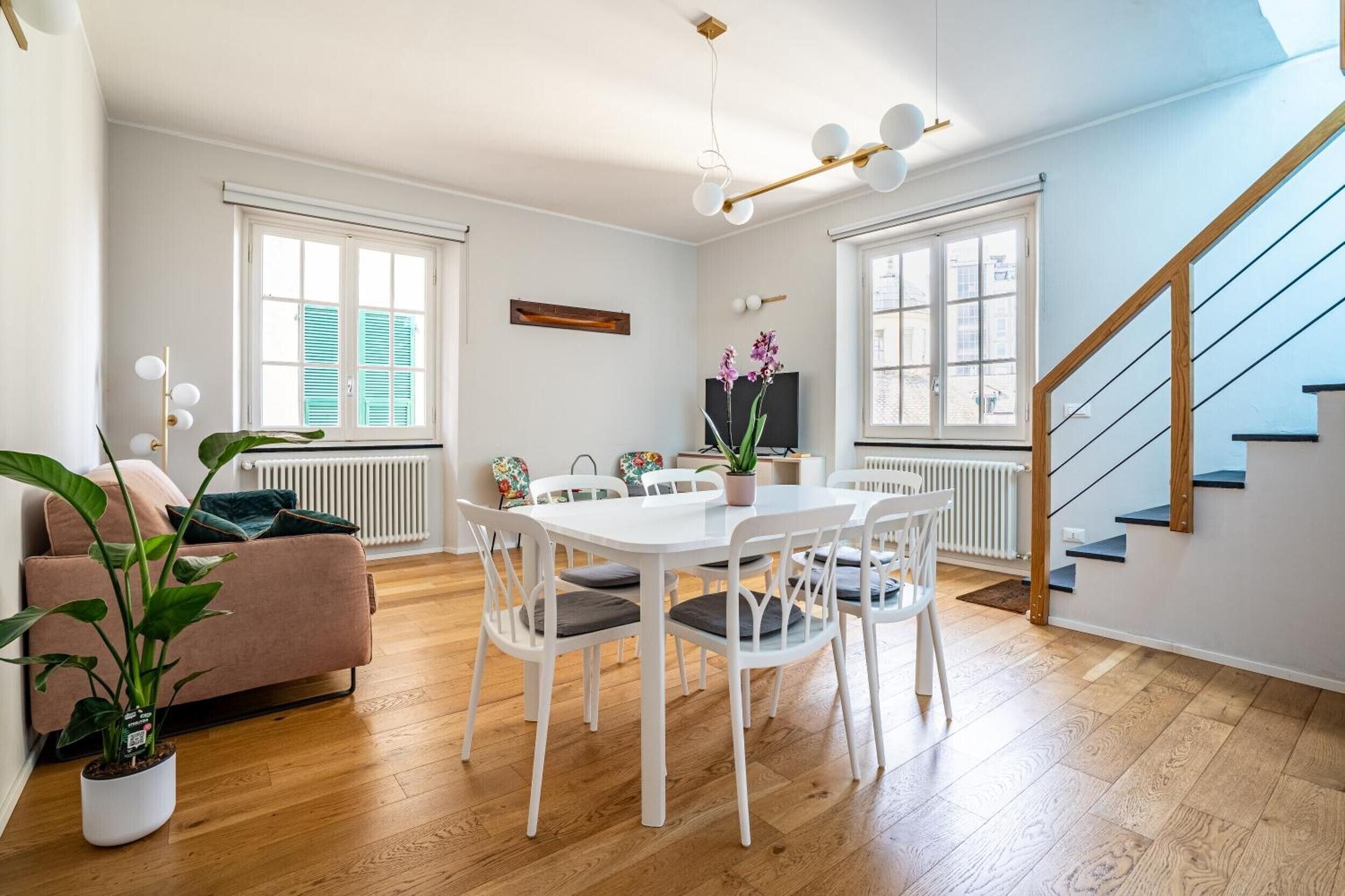 Een moderne woonkamer met een eethoek, houten vloeren, een trap en grote ramen.