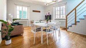 A modern living room with a dining area, wooden flooring, a staircase, and large windows. - Residenza Pellicceria – Rooftop Terrace in a Historic Palazzo dei Rolli (Genoa)