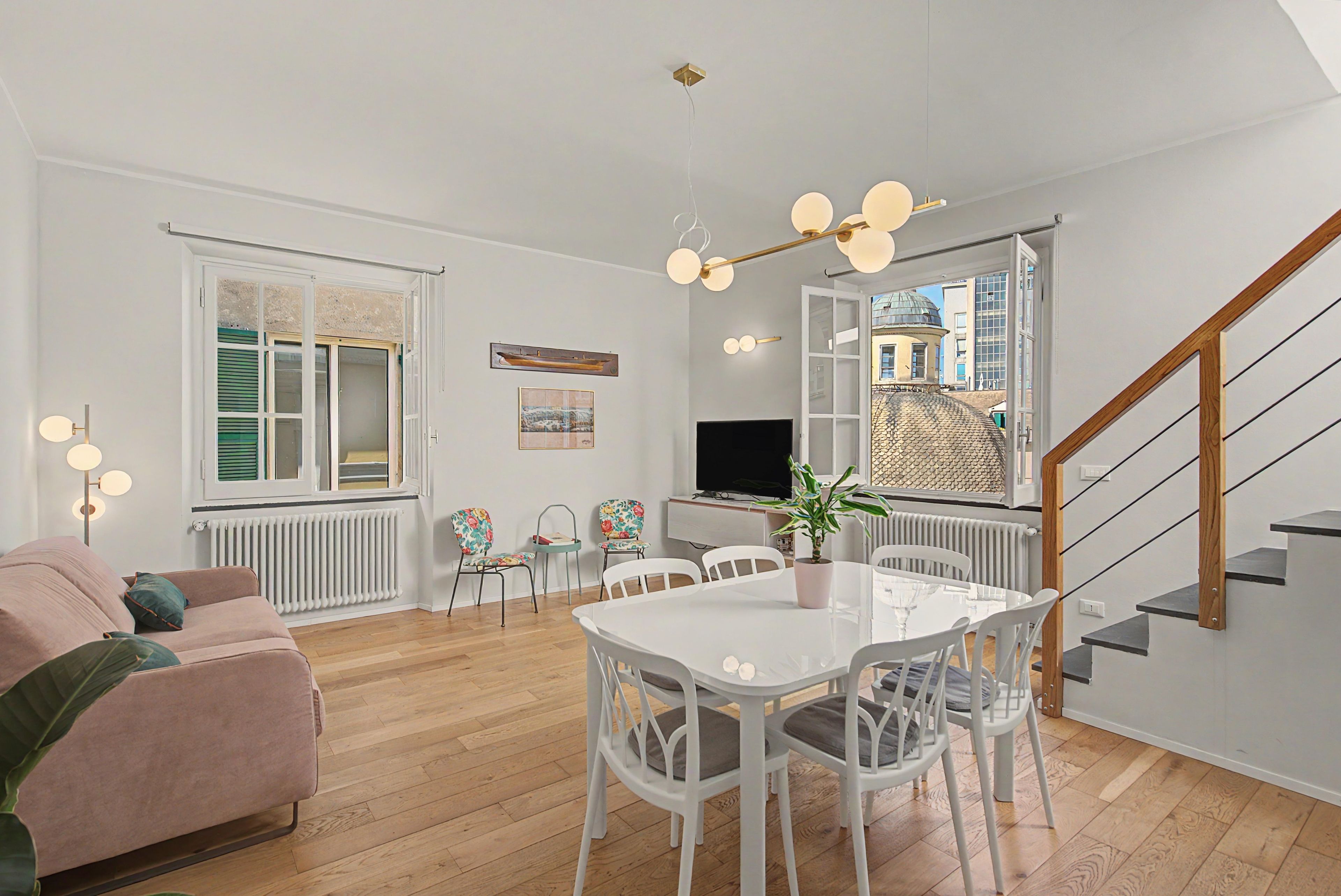 A modern living room with a sofa, dining table, chairs, and a staircase.