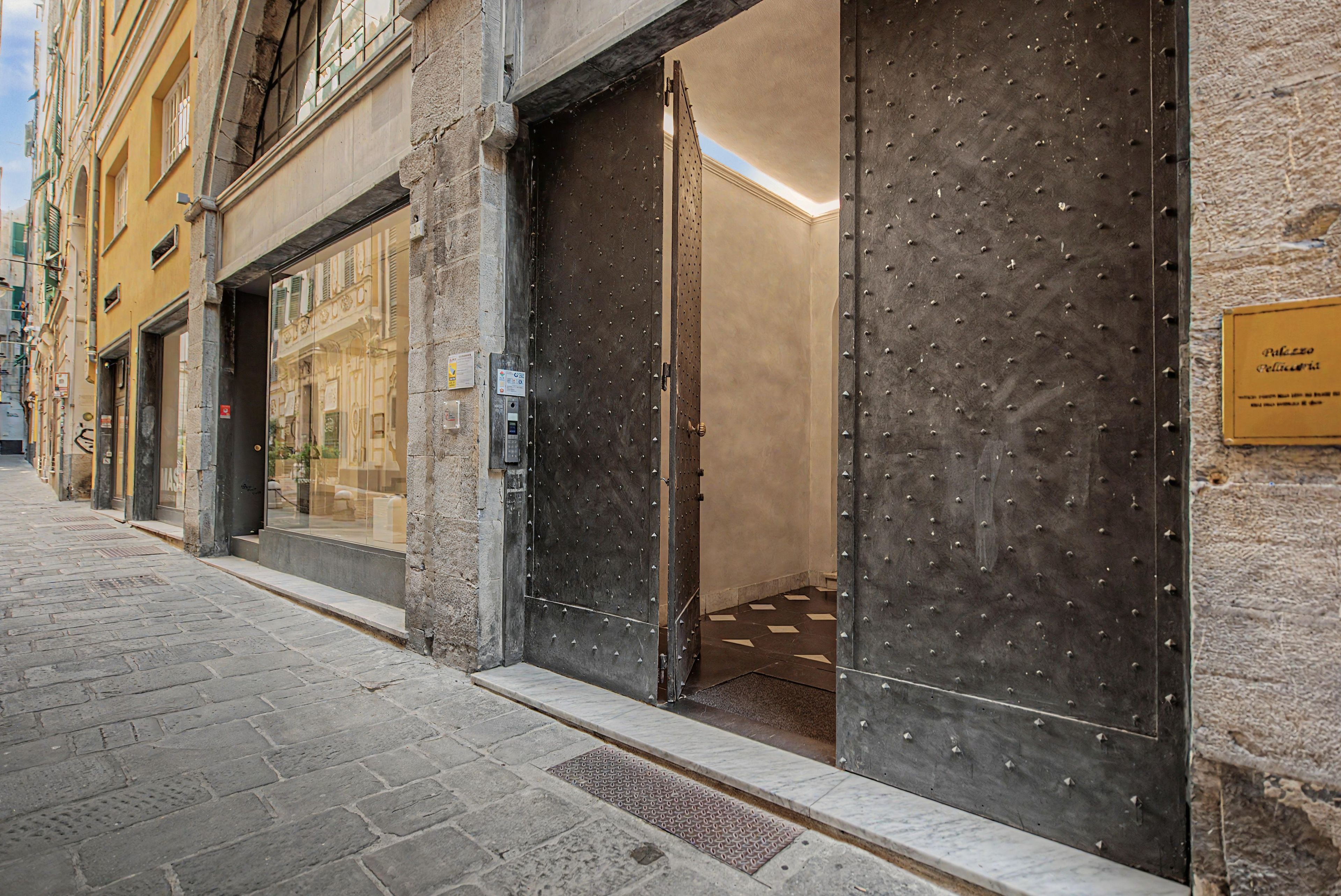 Une rue bordée de boutiques aux volets métalliques fermés, un trottoir pavé et un immeuble sur lequel on peut lire l’inscription « Palazzo Pellestrini ».