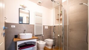 A modern bathroom with a glass shower enclosure, a sink with a wooden countertop, a bidet, and a toilet. - Residenza Pellicceria – Rooftop Terrace in a Historic Palazzo dei Rolli (Genoa)
