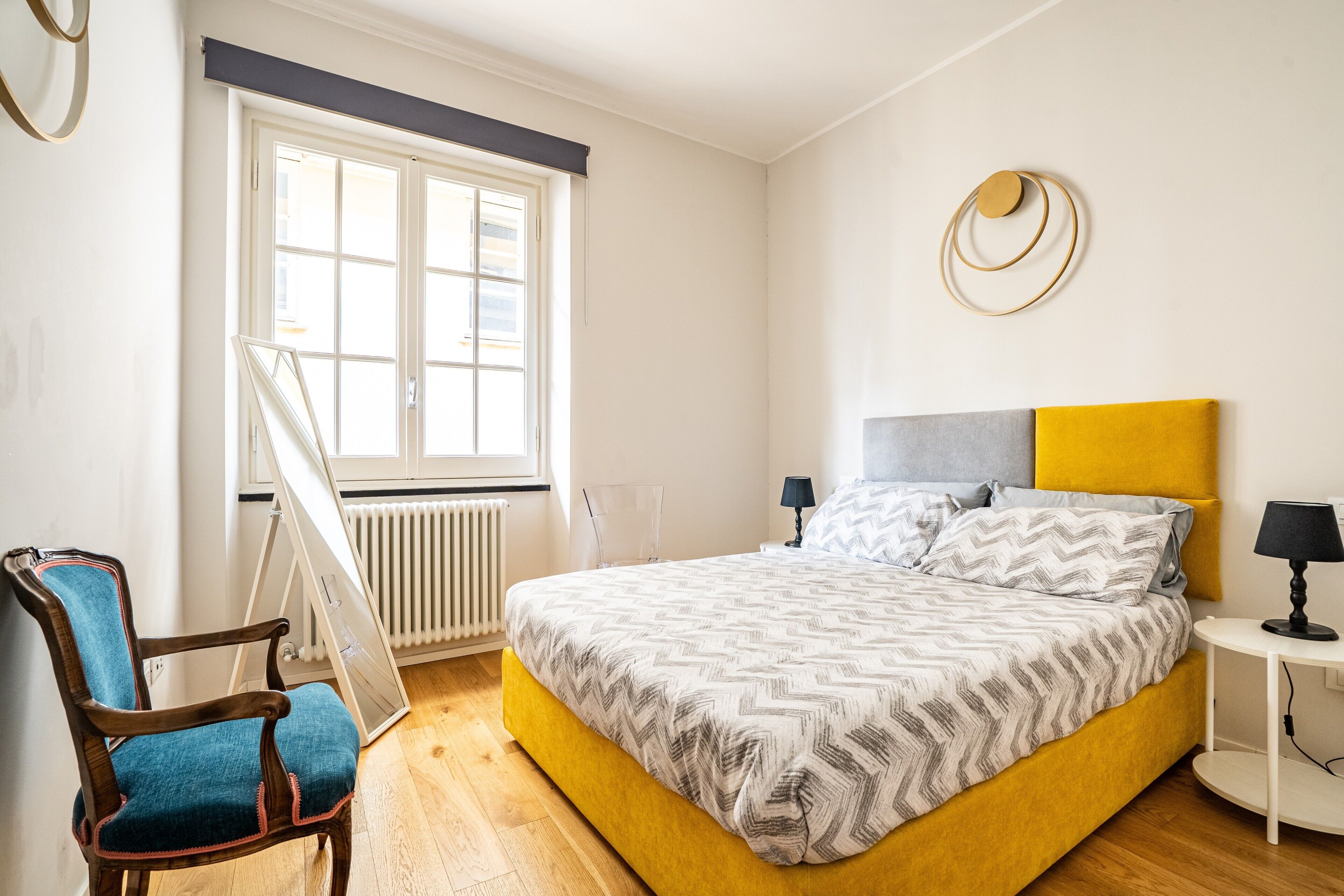 Een slaapkamer met een bed, een stoel, een nachtkastje, een lamp en een raam.