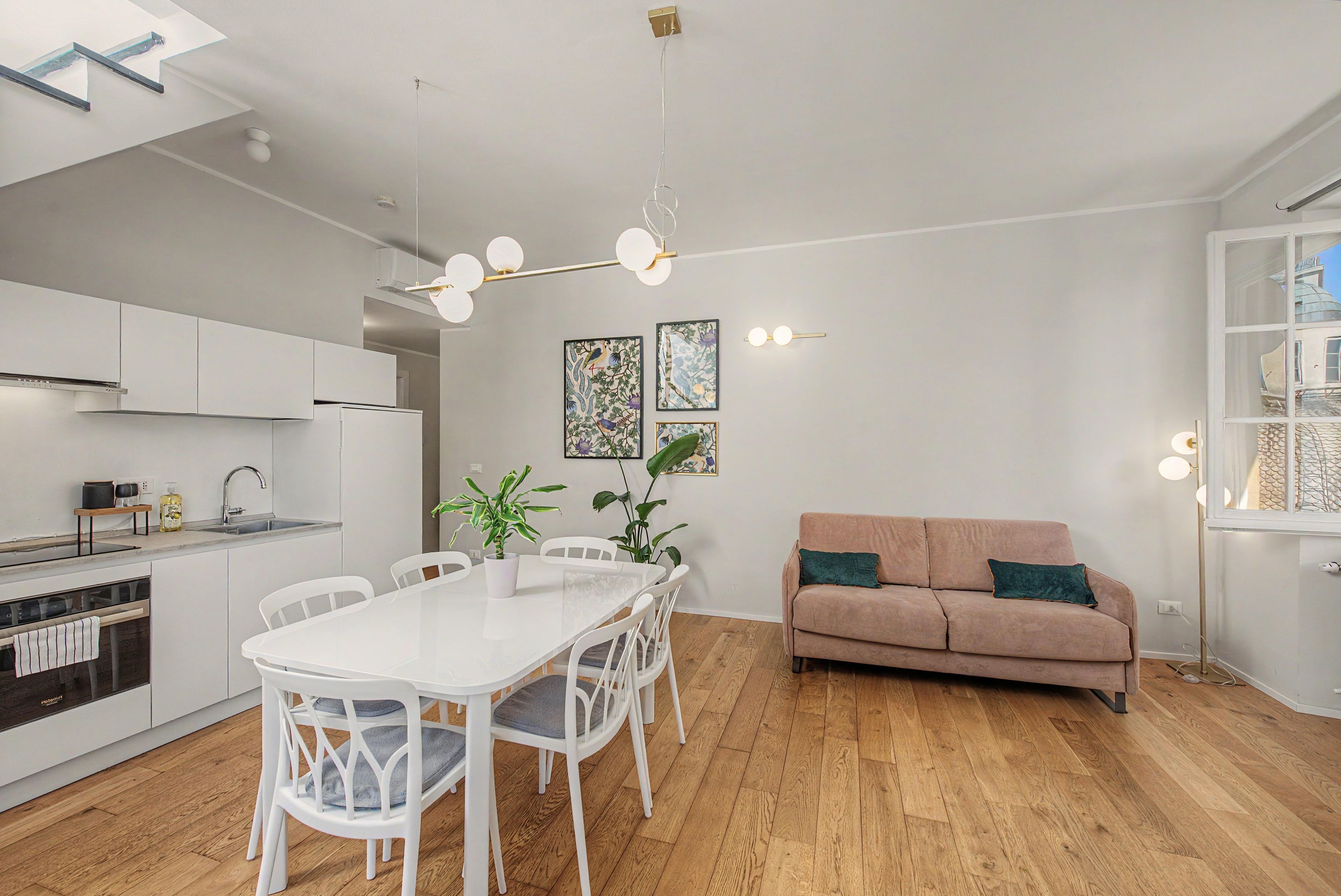 Eine moderne Küche mit weißen Schränken, einem Esstisch mit Stühlen, einer Couch und einer Deckenleuchte.