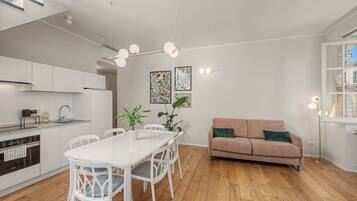 Eine moderne Küche mit weißen Schränken, einem Esstisch mit Stühlen, einer Couch und einer Deckenleuchte.