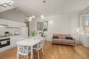 Una cucina moderna con mobili bianchi, un tavolo da pranzo con sedie, un divano e una lampada a sospensione.
