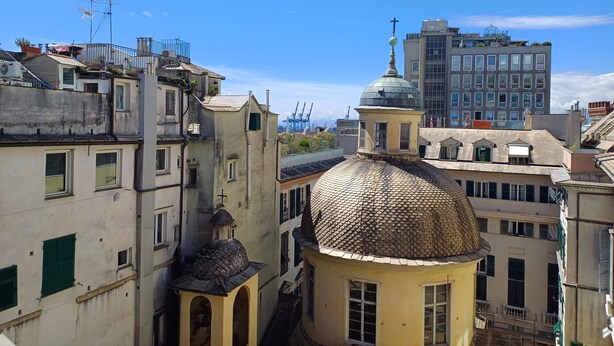 A cityscape with a mix of residential and commercial buildings, including a prominent church with a dome and a cross on top. - Residenza Pellicceria – Rooftop Terrace in a Historic Palazzo dei Rolli (Genoa)