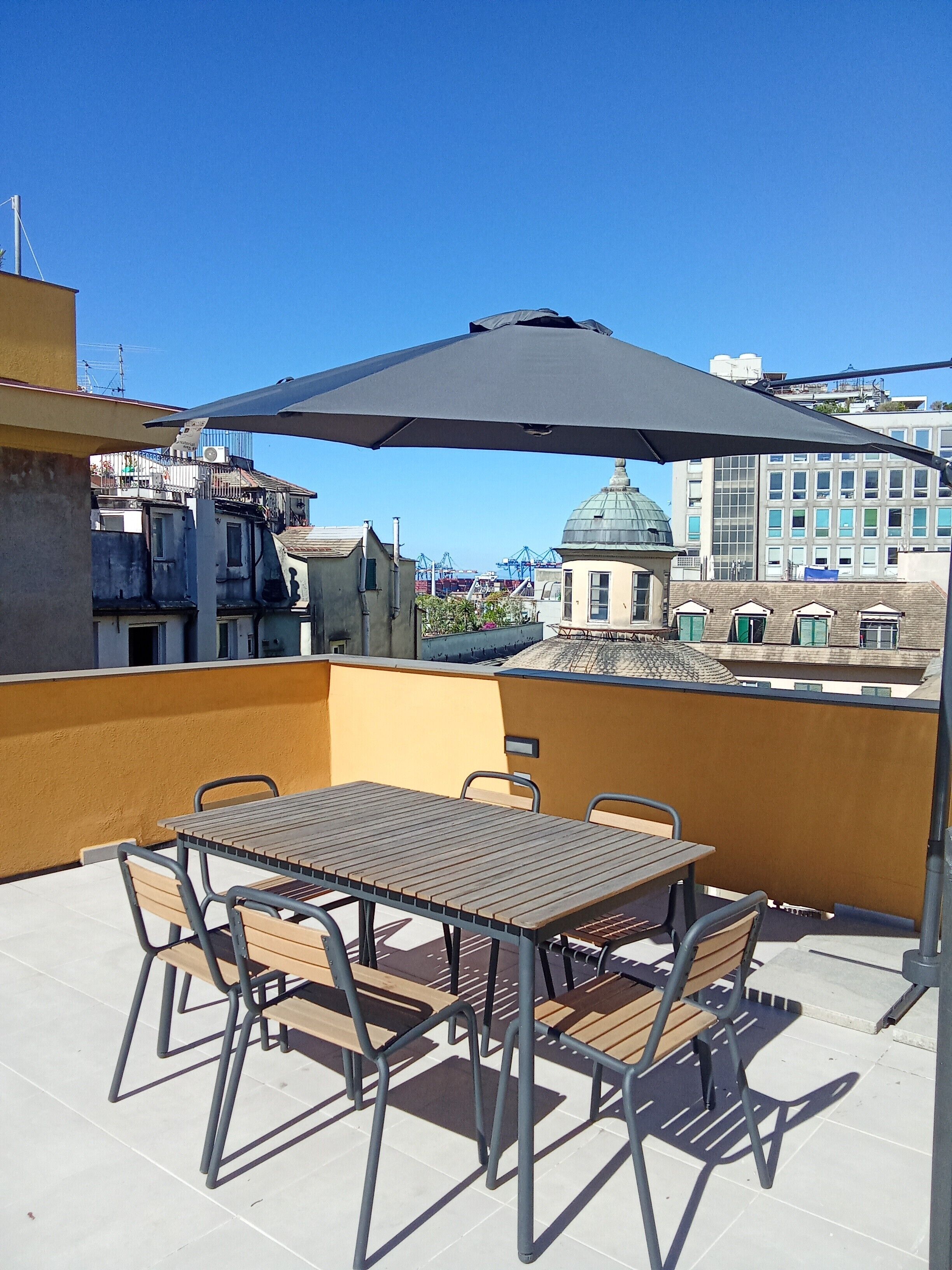 Een dakterras met een tafel, stoelen, een grote parasol en uitzicht op de stad.