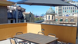 A rooftop terrace with a table and chairs, a large umbrella, and a view of the cityscape. - Residenza Pellicceria – Rooftop Terrace in a Historic Palazzo dei Rolli (Genoa)