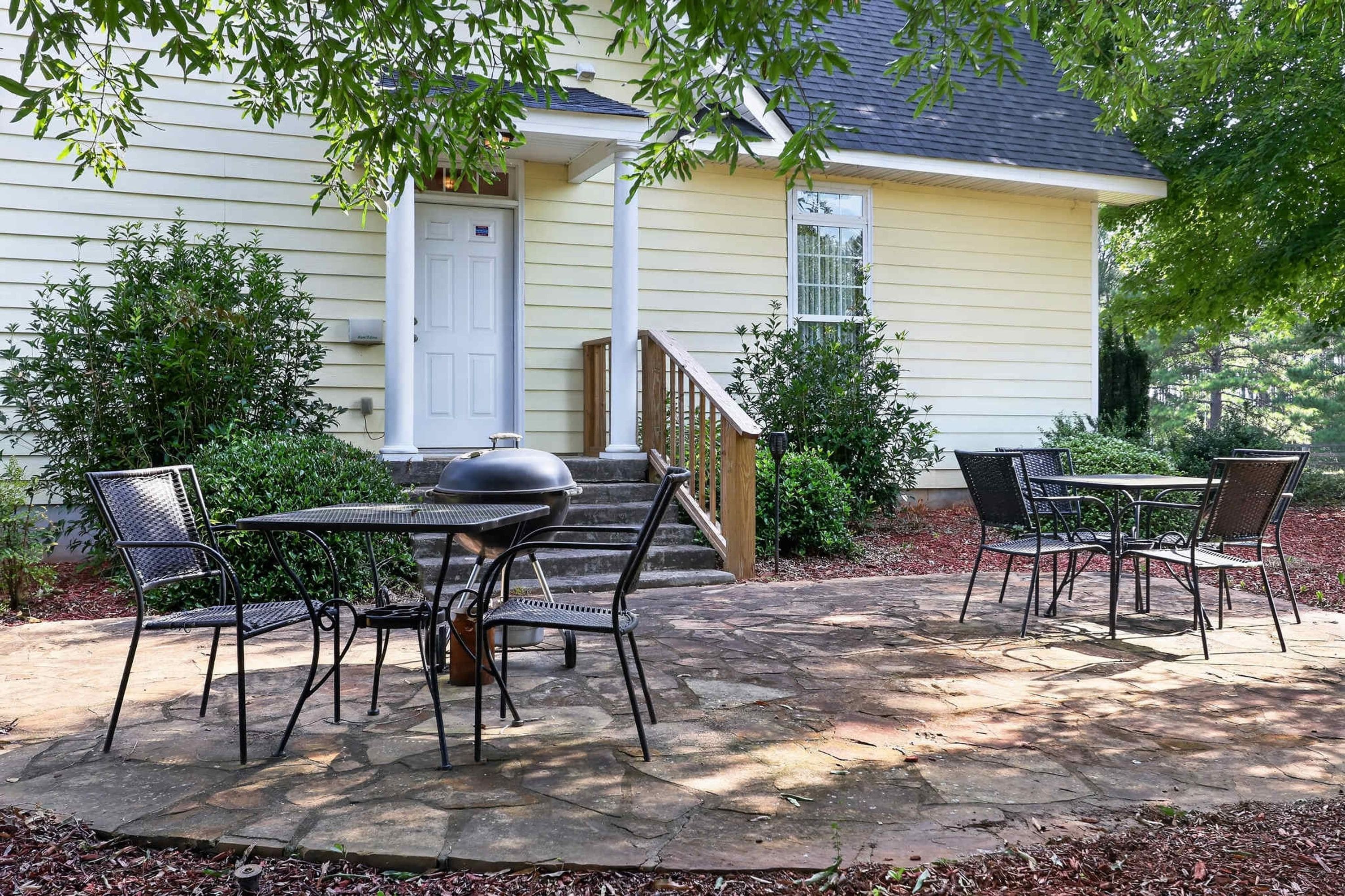 A patio with outdoor furniture, a grill, and a house with a front door and steps.