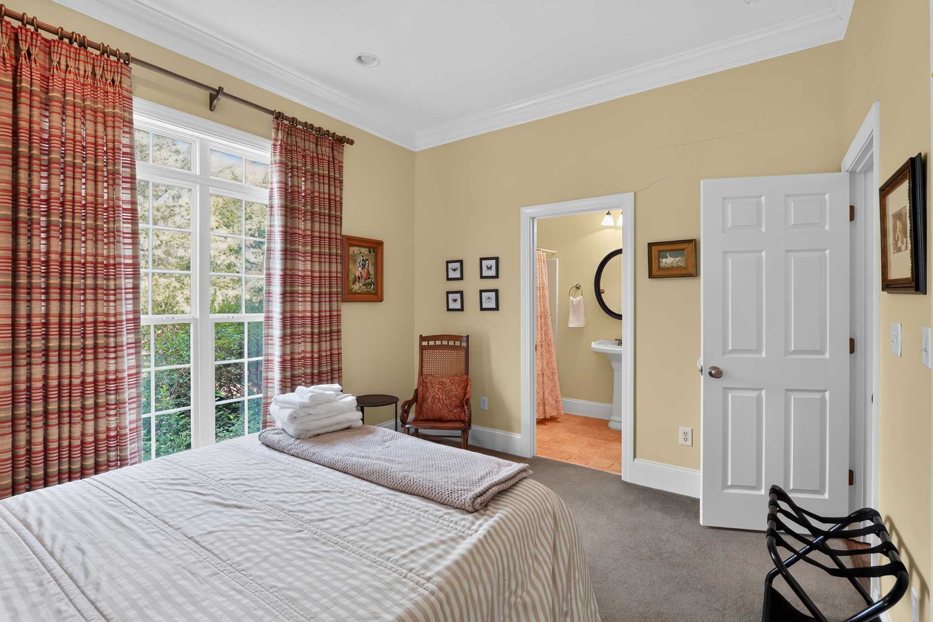 A hotel room with a large bed, a chair, a door, and a view of the outdoors.
