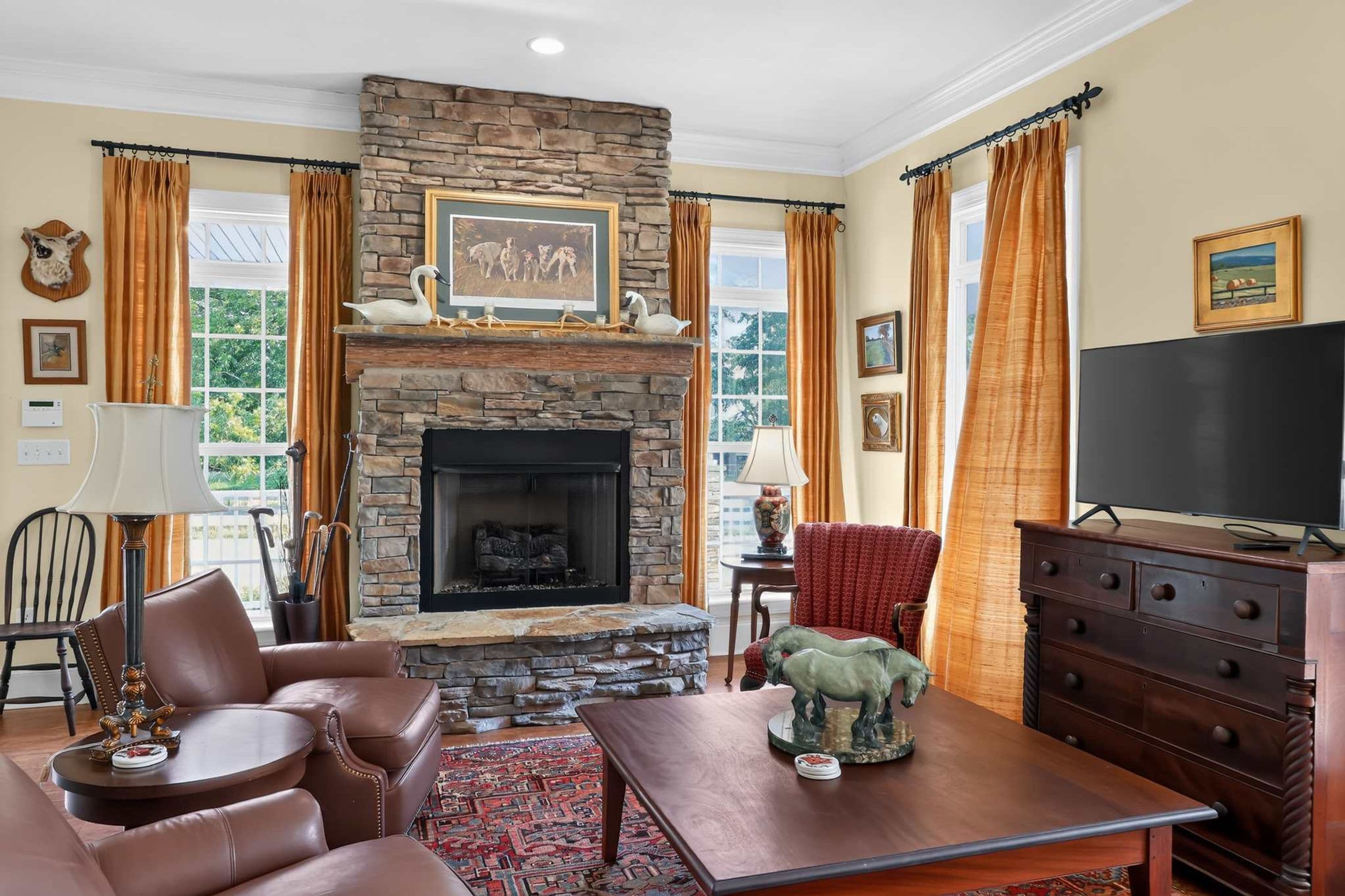 A living room with a stone fireplace, leather furniture, a television, and a large window with curtains.