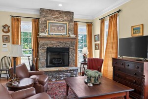 A living room with a stone fireplace, leather furniture, a television, and a large window with curtains.
