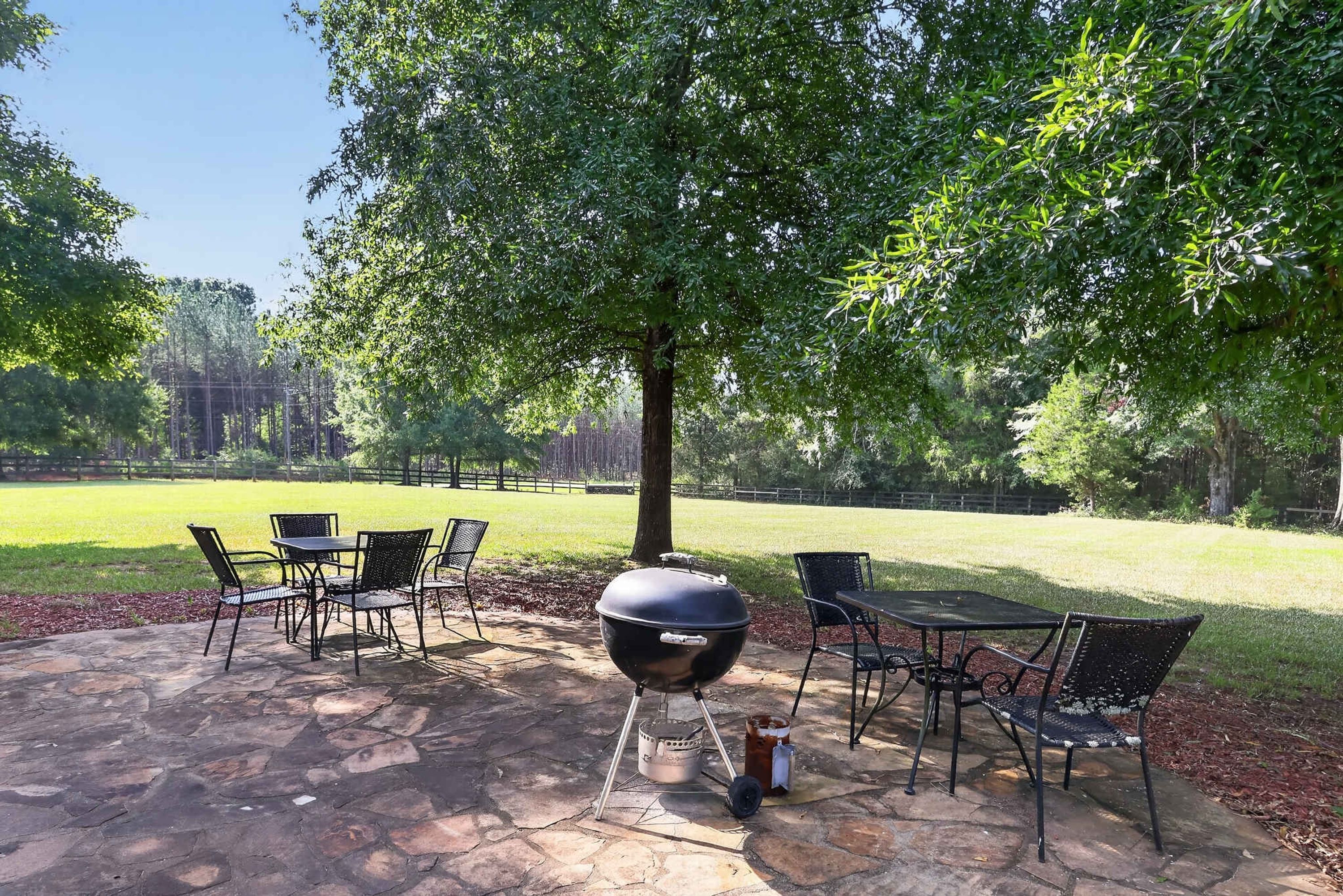 Un patio al aire libre con suelo de piedra, sillas de metal, una mesa y una parrilla.