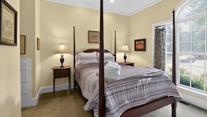Uma cama com dossel com colcha listrada, duas luminárias de cabeceira e uma janela grande com cortinas.
