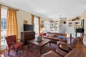 Een woonkamer met een bank, fauteuils, een salontafel, een televisie en een open haard.