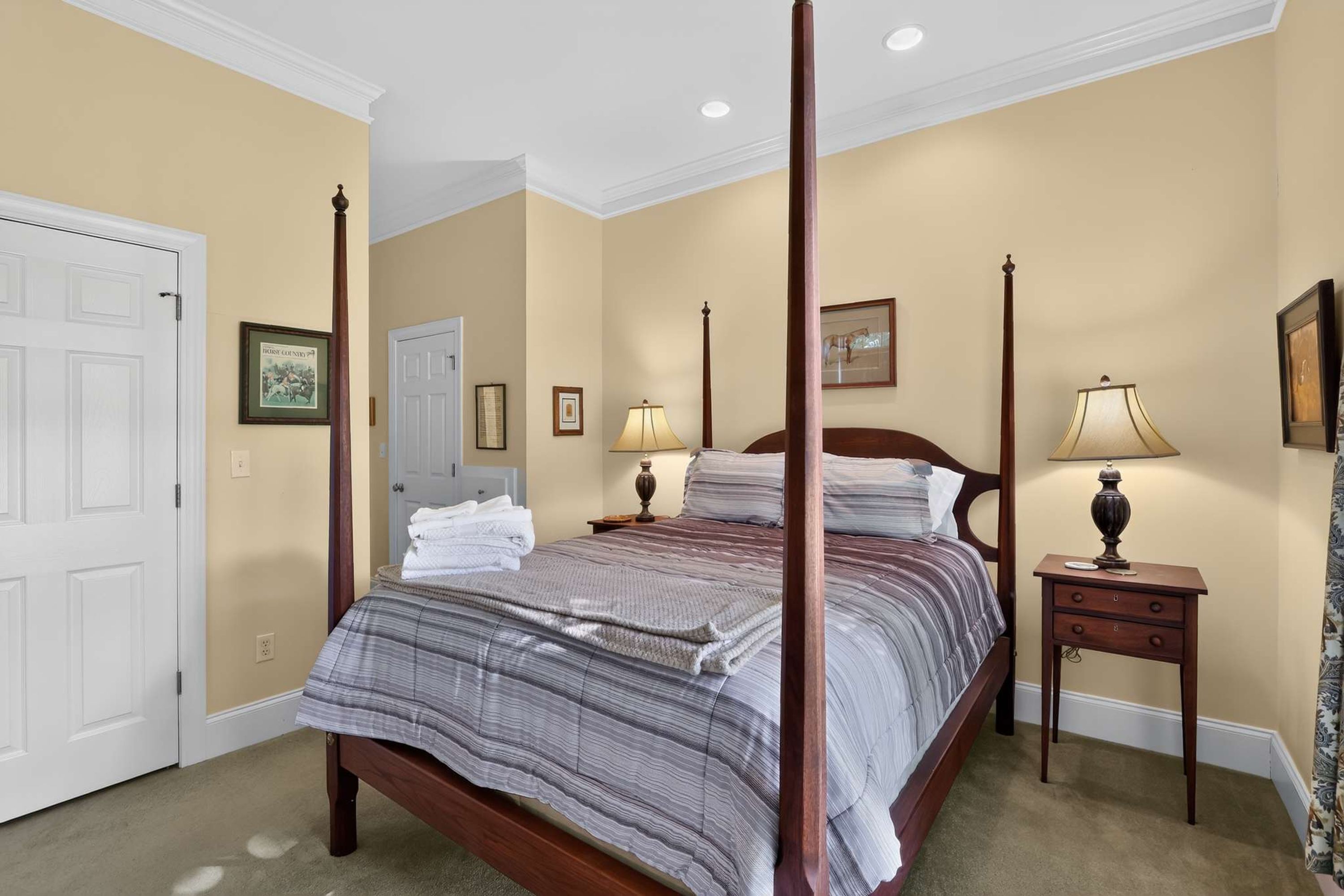 Un lit à baldaquin avec une couvre-lit à rayures, deux tables de chevet avec des lampes et une porte ornée d’un tableau encadré.