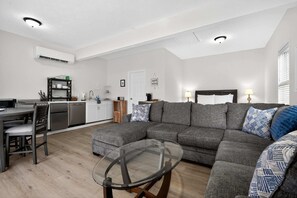 A modern living room with a sectional sofa, a glass coffee table, and a dining area with a kitchen in the background. - Augusta Carriage House Cozy Retreat w Kitchen (Augusta)