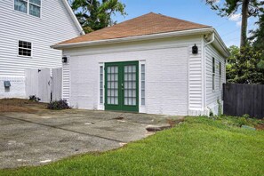 A small, single-story building with a green door and white siding, adjacent to a larger house with a sloped roof. - Augusta Carriage House Cozy Retreat w Kitchen (Augusta)