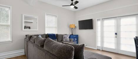A living room with a sectional sofa, a ceiling fan, a flat-screen TV, and a sliding glass door.