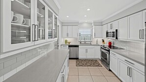 A modern kitchen with white cabinetry, stainless steel appliances, and a central island. - Coastal Naples Park Getaway - Garden Grill Beach Nearby (Naples)