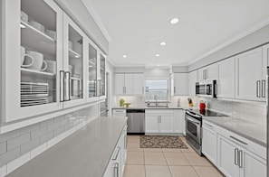 A modern kitchen with white cabinetry, stainless steel appliances, and a central island. - Coastal Naples Park Getaway - Garden Grill Beach Nearby (Naples)