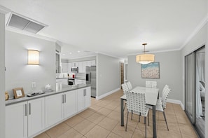 A modern kitchen with white cabinetry, a central island, and a dining area with a table and chairs.