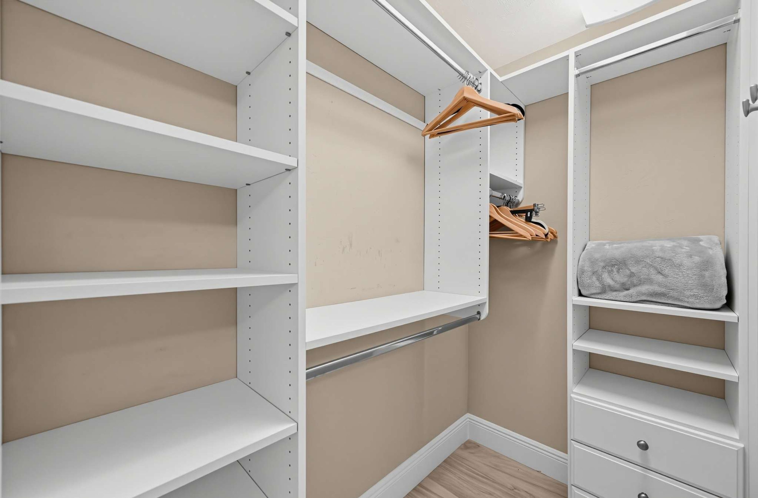 Un armario vestidor con estanterías blancas, un perchero de madera y una toalla gris.