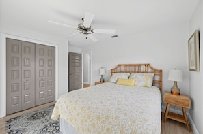 A bedroom with a bed, bedside tables, a ceiling fan, and a door. - Coastal Naples Park Getaway - Garden Grill Beach Nearby (Naples)