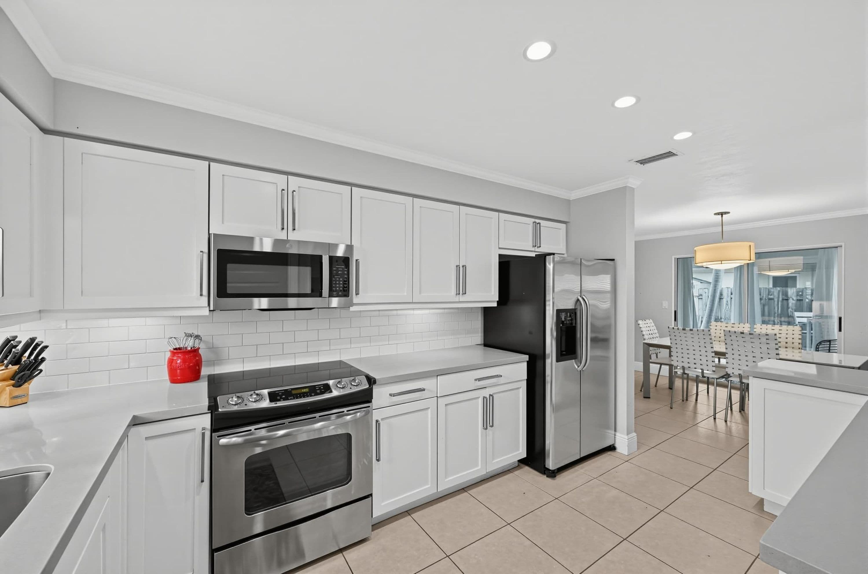 A modern kitchen with white cabinetry, stainless steel appliances, and a dining area with a view.