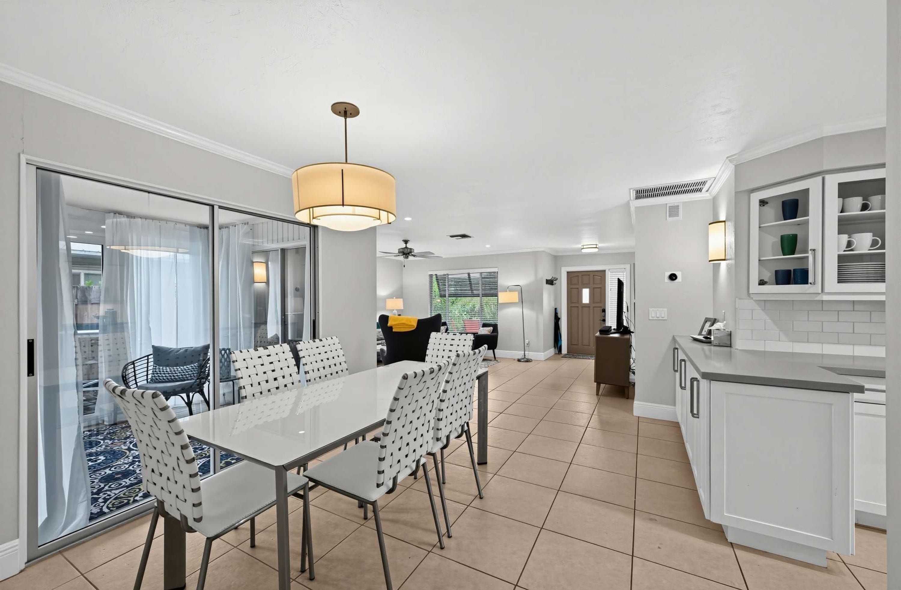 A modern kitchen with white cabinetry, a dining area with a glass partition, and a view of a garden.