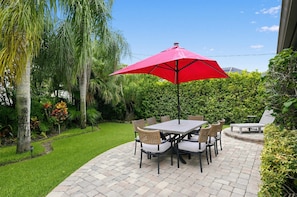 A patio with a table and chairs, surrounded by lush greenery and a red umbrella. - Coastal Naples Park Getaway - Garden Grill Beach Nearby (Naples)