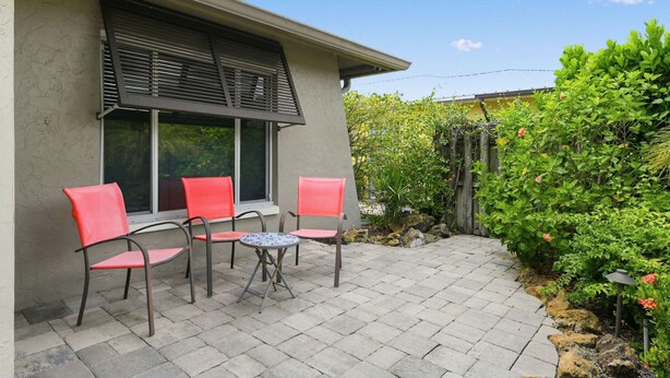 A patio with four chairs and a small table, a window with blinds, and a garden with various plants. - Coastal Naples Park Getaway - Garden Grill Beach Nearby (Naples)
